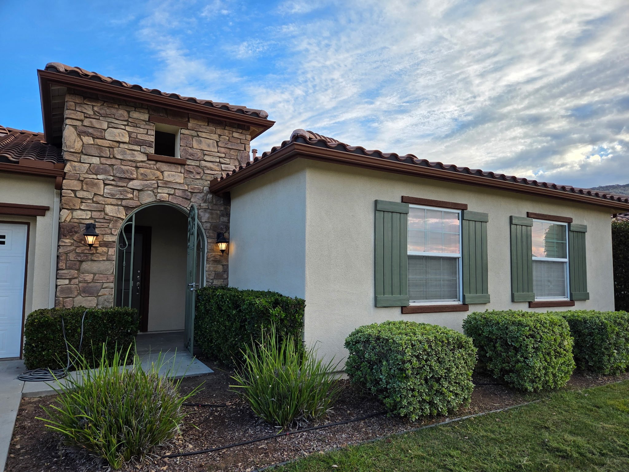 Stone veneer entry tower with arched iron gate and repainted brown fascia by AAA Painting in the Inland Empire, CA